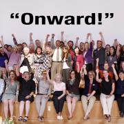 Dean Williams surrounded by former and current faculty and staff with arms raised under the word Onward.