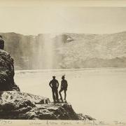 Two people standing on a rock outcropping over a lake.