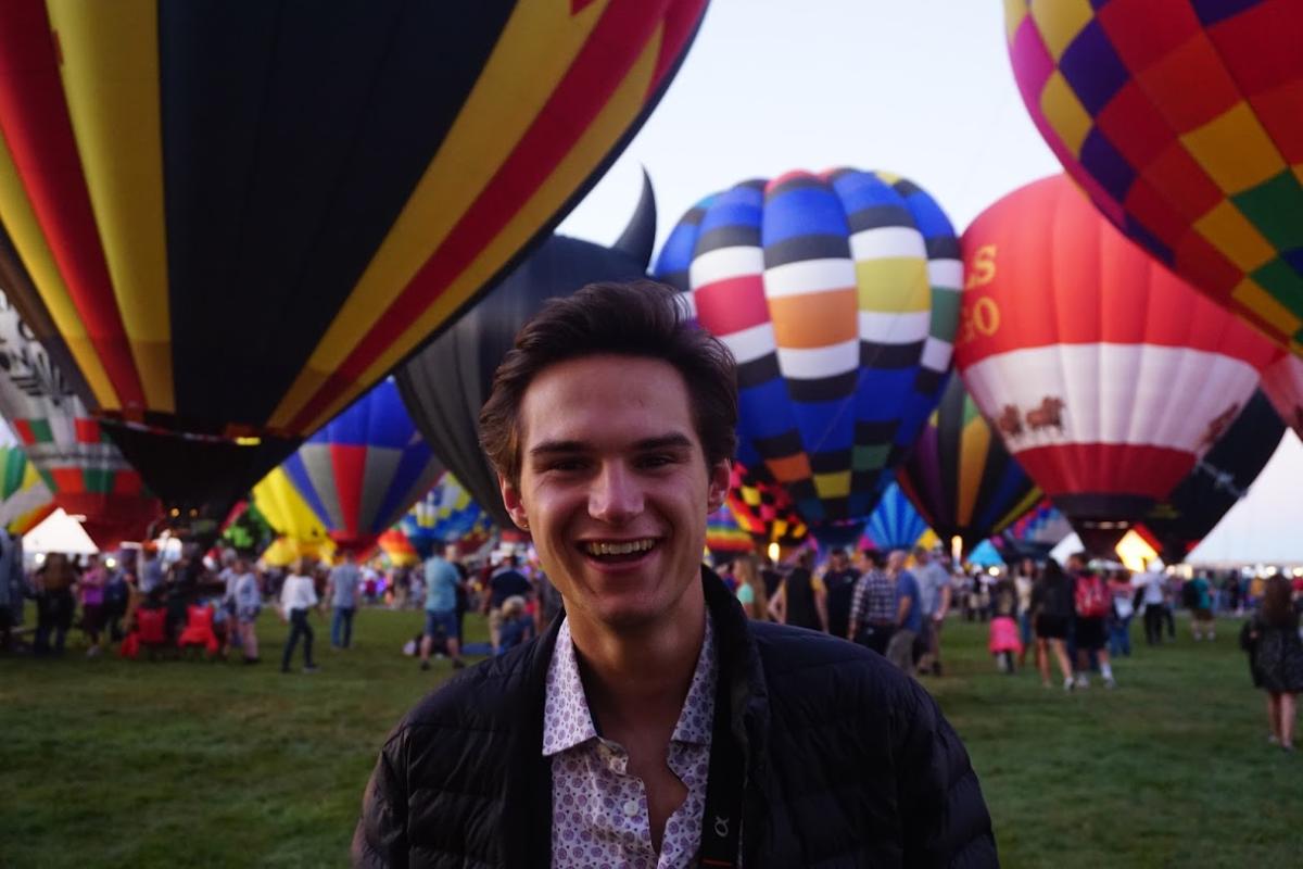 A person smiles at the camera in front of grounded hot air balloons.