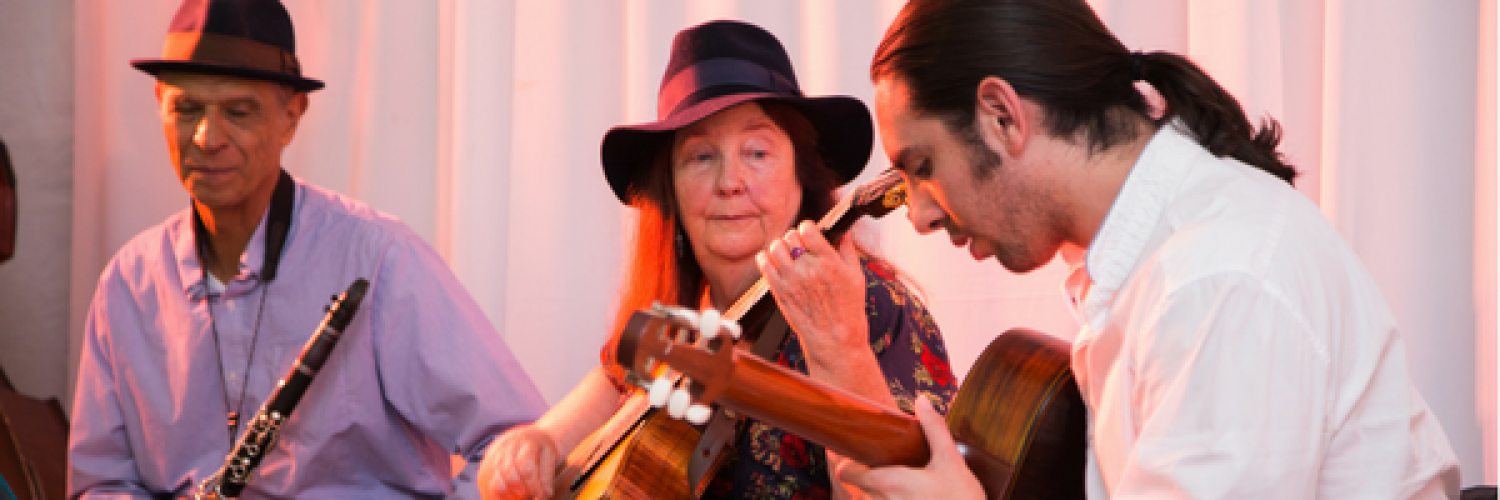Three musicians sitting and playing two guitars and a clarinet