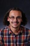 Professional photo of Jeremy Diaz, wearing glasses and plaid shirt against blue background