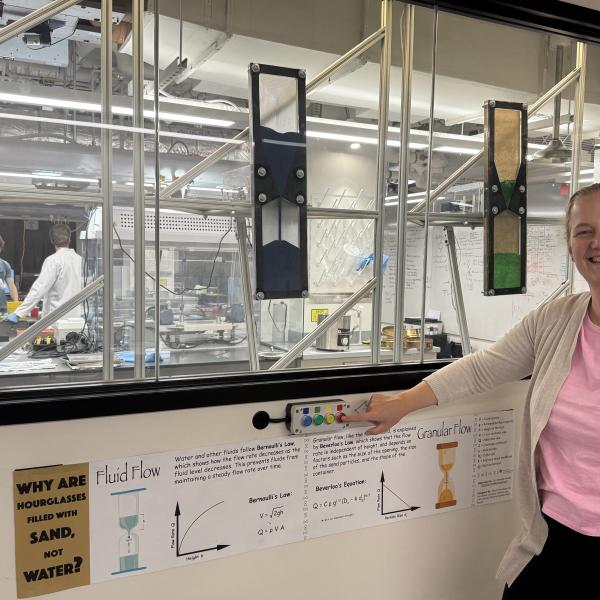woman standing in front of motorized hourglass display in lab window