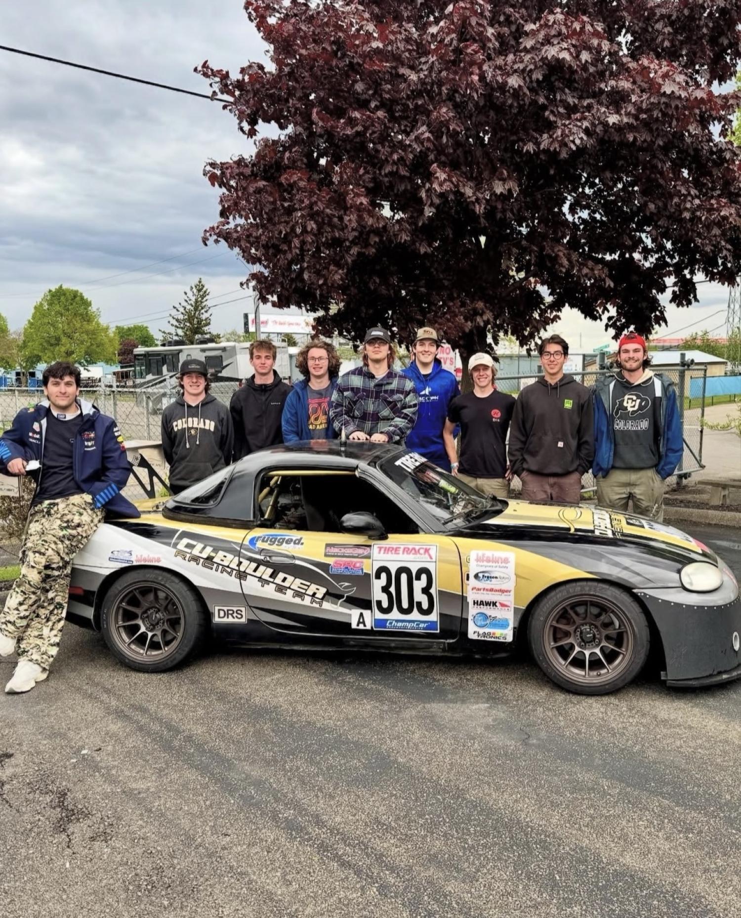 a group of male students standing outside, posing for group photo behind endurance racing vehicle with CU Boulder branding