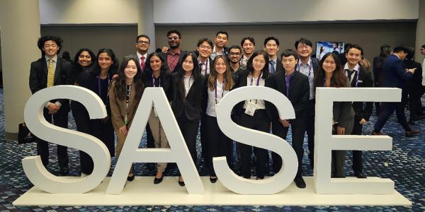The student chapter poses for a group photo behind a SASE sign in a hotel lobby
