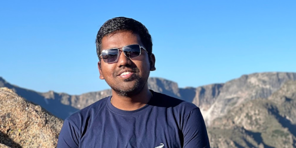 Closeup of male graduate student wearing sunglasses with bright blue sky in the background.