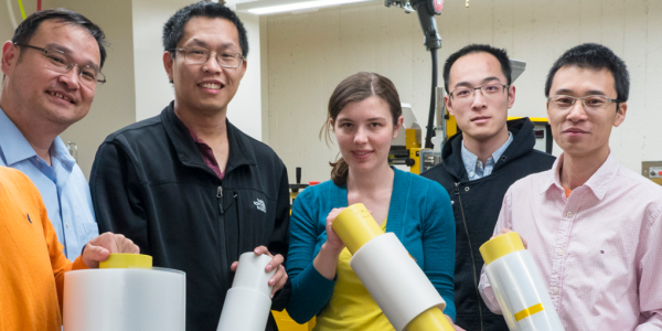 Ronggui Yang and Xiaobo Yin in a lab with a group of students holding rolls of a film material.