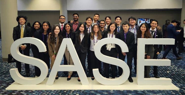The student chapter poses for a group photo behind a SASE sign in a hotel lobby