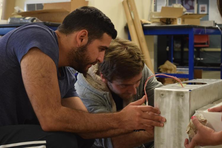 Two students working on a cooler device for long term storage of medical supplies following natural disasters.