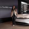Carlota stands next to a white Lucid car. The company's logo is shown on the showroom wall behind her