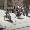 Two students race their vehicles down a sidewalk as their classmates look on
