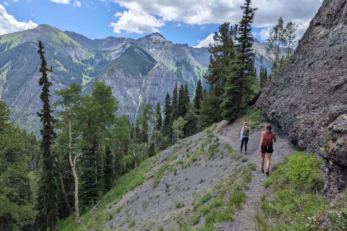 Two people walking on a trail on the side of a mountain.