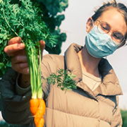 Masked farmworker holding up carrot