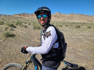 Nicholas Kellaris on a mountain bike with helmet and sunglasses in the desert