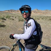 Nicholas Kellaris on a mountain bike with helmet and sunglasses in the desert