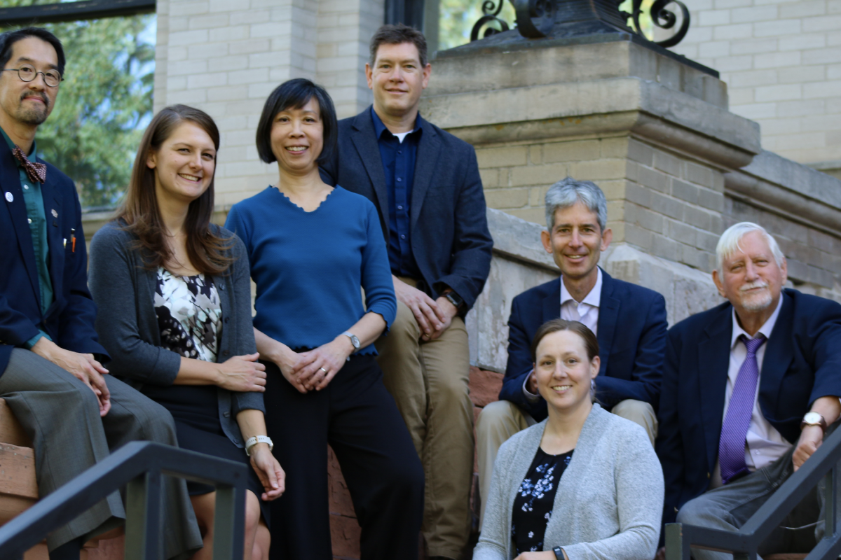 Seven music theory faculty sitting on steps for a group photo wearing casual professional attire.