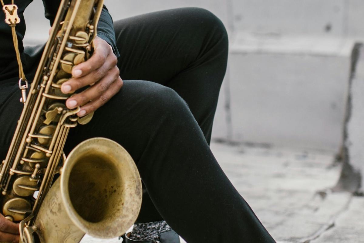 A person seated on the ground playing the saxophone.