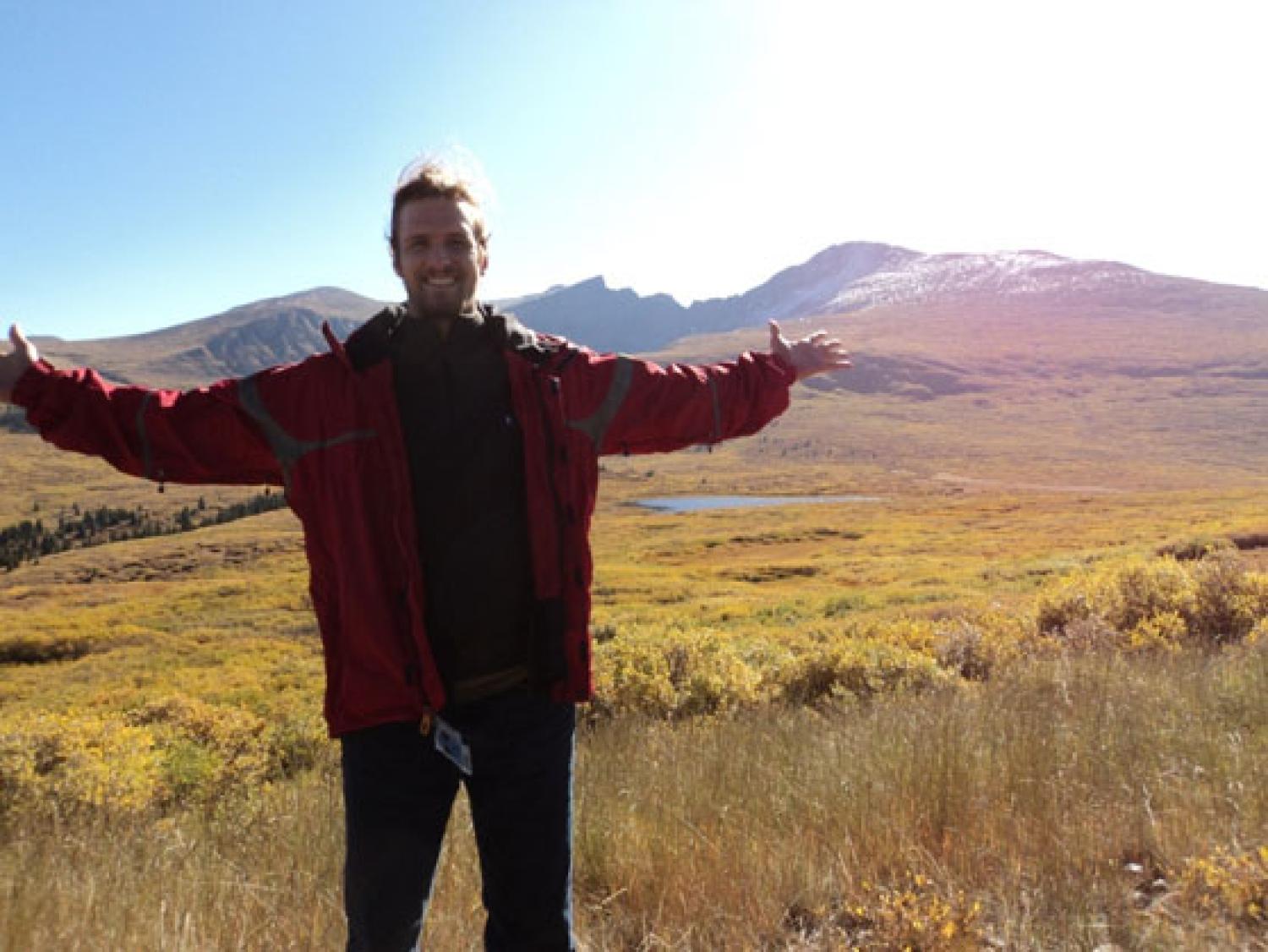 a grad student spreads his arms in a meadow