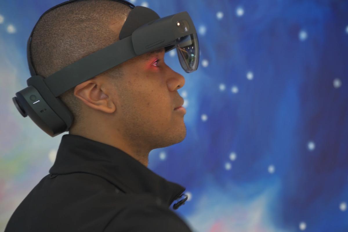 A man wearing a virtual reality headset in front of a space-themed mural.