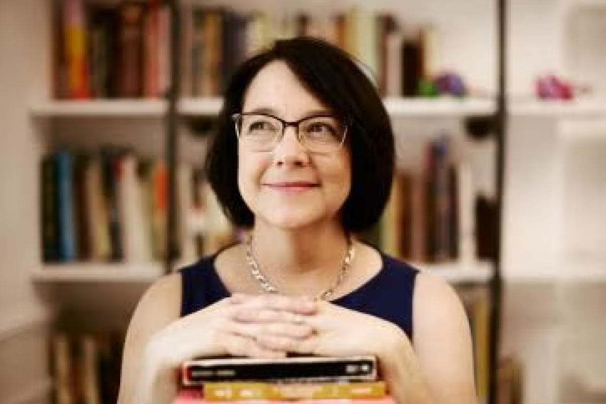 A woman with short dark hair smiling while her eyes look slightly away from the camera. Her hands are resting on a stack of books.