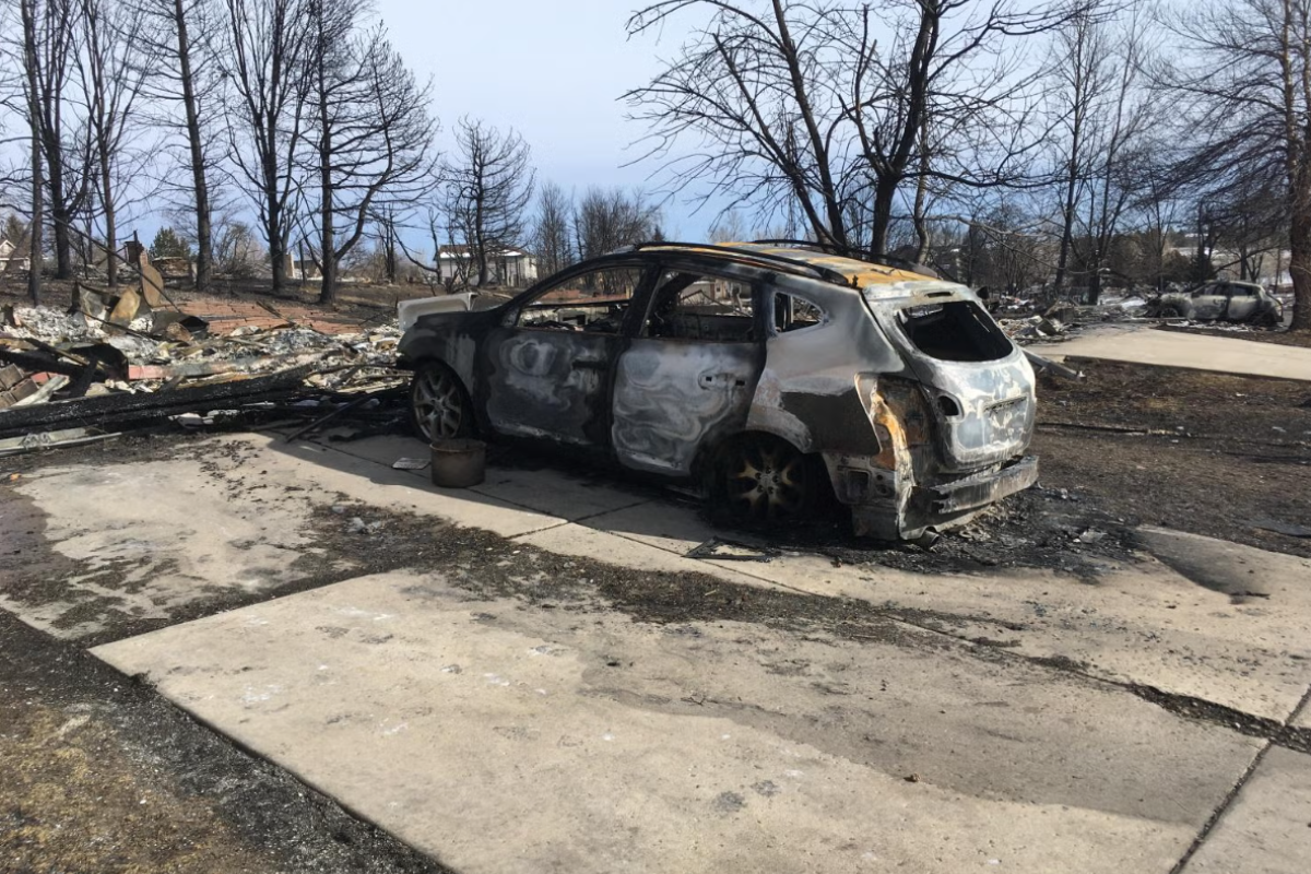 A burnt shell of a car parking in the driveway of a home destroyed by fire.