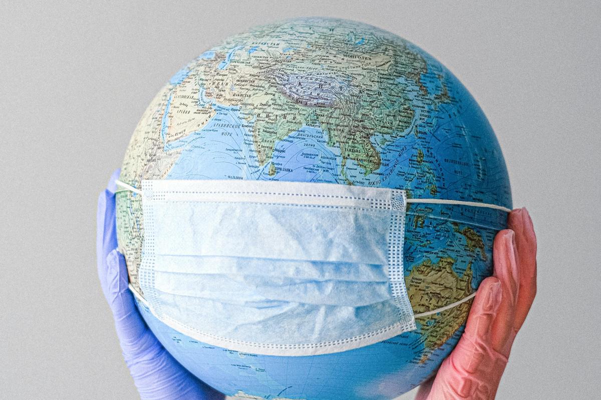 A surgical mask placed over a globe. The globe is being held up by two gloved hands.