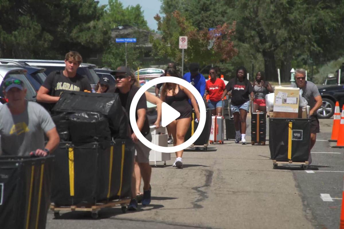 Parents and students moving items from cars into boxes with a play button superimposed on top of the image.