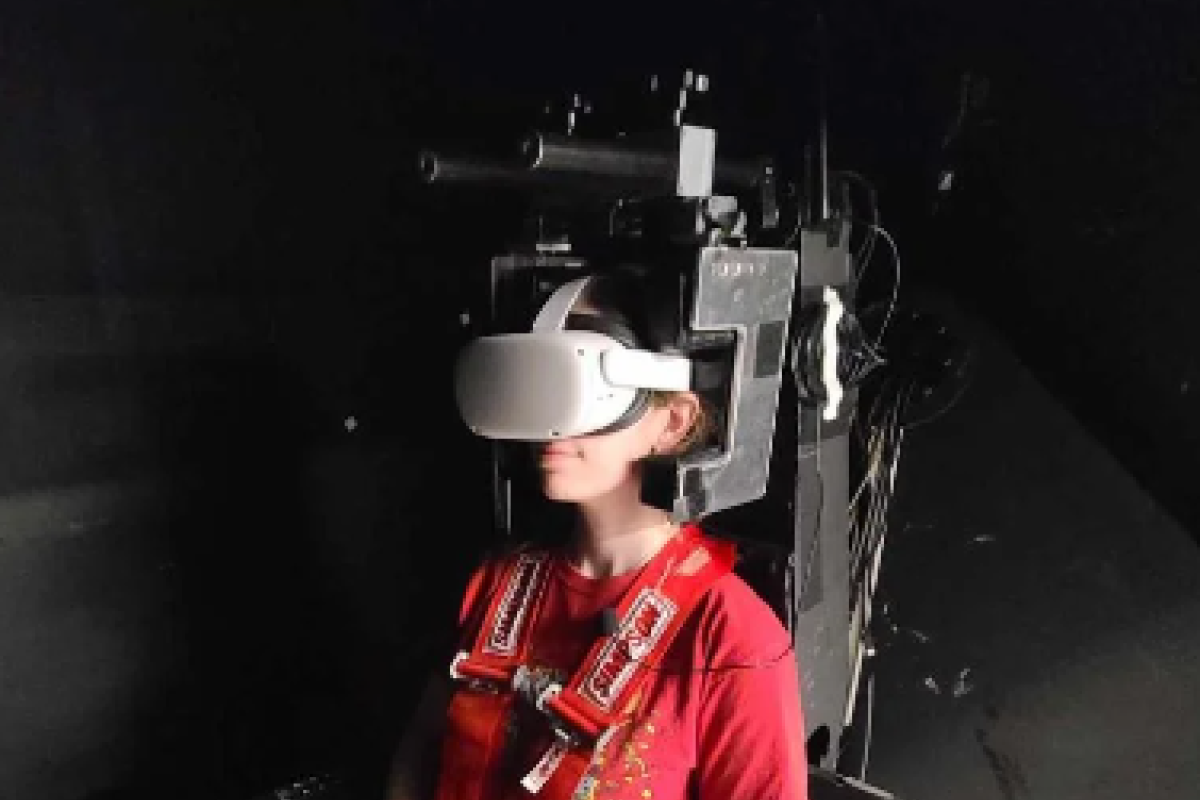 A students wears a virtual reality headset, sitting in a machine that mimics the motion of ocean waves.