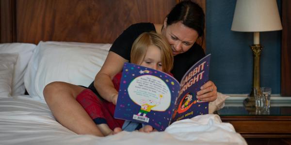 Caregiver and child sitting in bed reading bedtime story