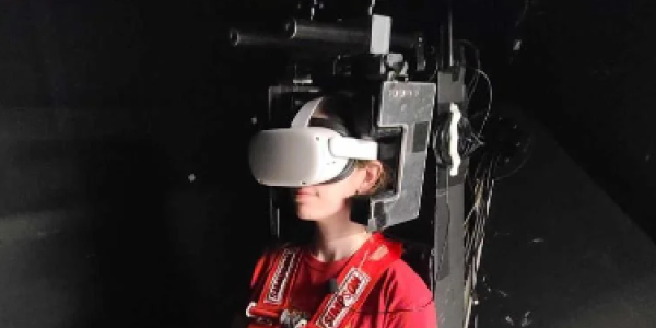 A students wears a virtual reality headset, sitting in a machine that mimics the motion of ocean waves. 