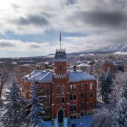 A photo of Old Main and CU Boulder campus taken from drone. There is snow on the ground and buildings.