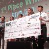 A diverse team of students stands on stage with their giant prize-winning check, the air is full of confetti, their joy is infectious