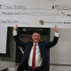 Grinning man stands with a giant check for $50,000 held over his head