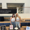 Two young women stand at a table with sample snacks on it