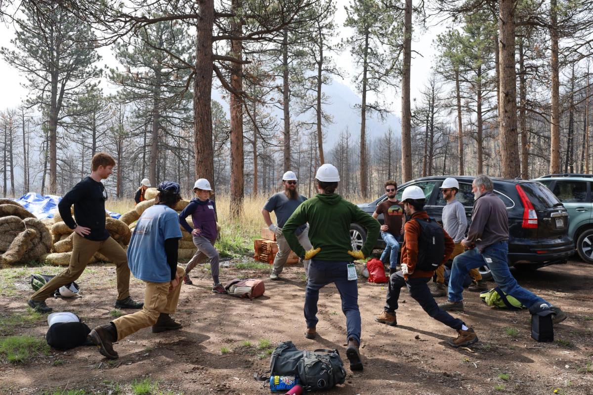 A group of volunteers do lunges in a circle with hard hats on