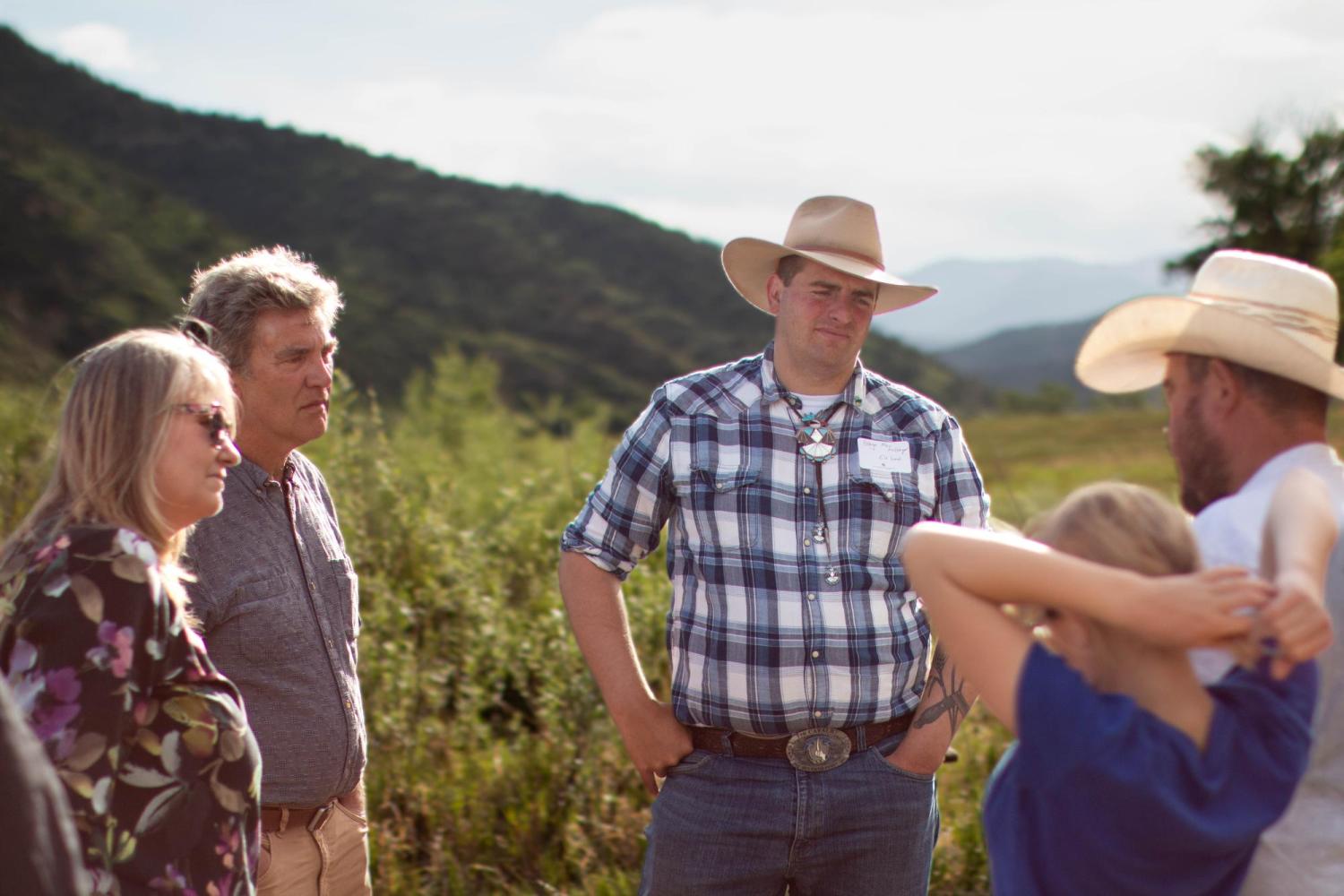 a group of people converse outside with mountains in the background
