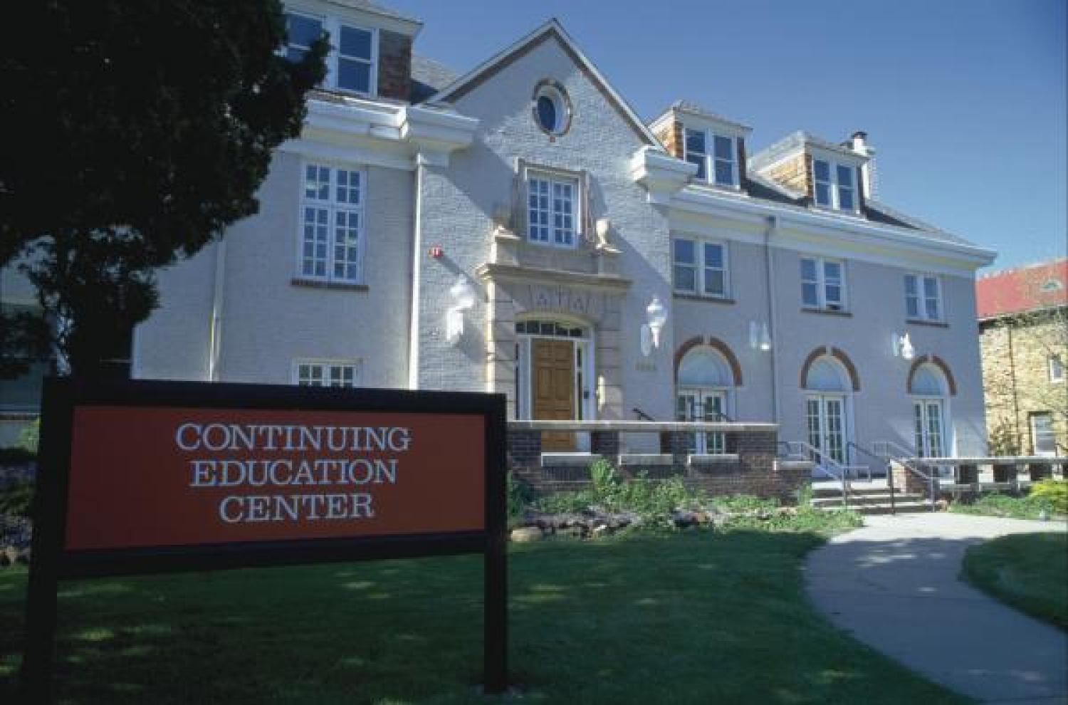 Large white building on a sunny day with a red sign in front that reads "Continuing Education"