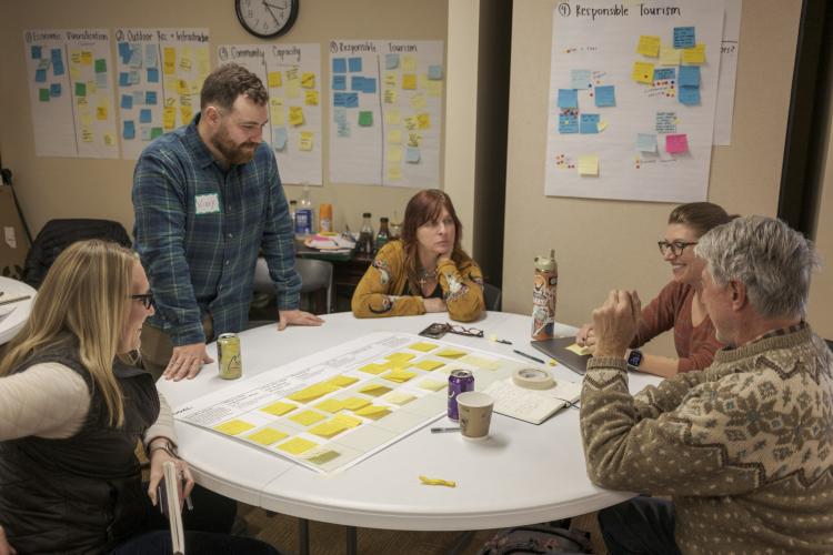 People sit around a white table and talk. On the table are a bunch of yellow sticky notes laid out in rows.
