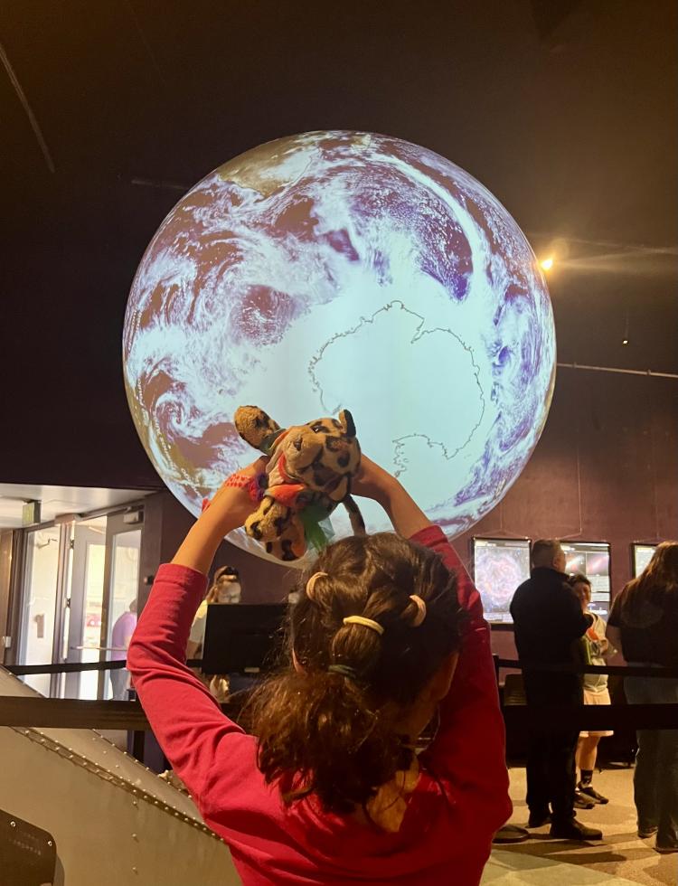 a young girl holds up a stuffed jaguar to a large projector moon at the Fiske Planetarium
