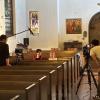 A filming crew surround two children seated in a church pew