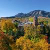 An aerial shot of Old Main on CU Boulder campus surrounded by trees with leaves turning to orange, red, and yellow with the flatirons in the background