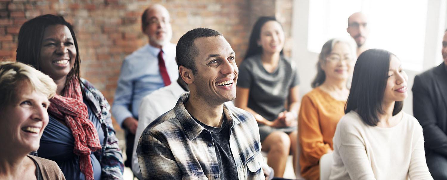 Group of people in a seminar setting sitting down and smiling.
