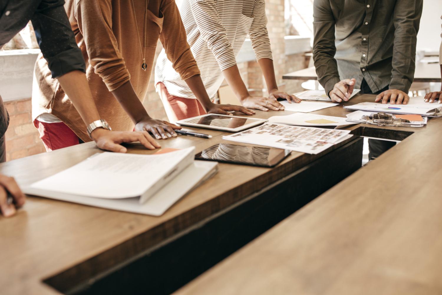 Group of people reviewing work laid out on a table.