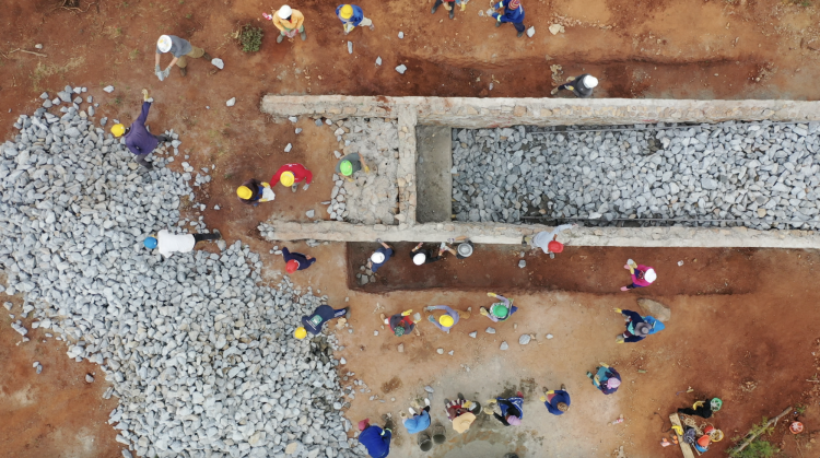Drone view of 15+ people moving rocks into the ramp