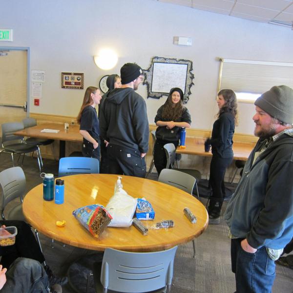 Two Scientists talking with five people on the janitorial staff in the cafeteria
