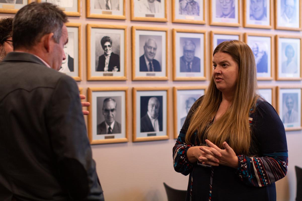A woman is in conversation with two men who have their backs turned to the camera.