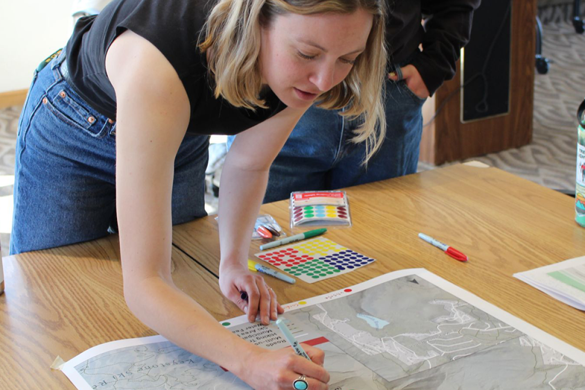 A college aged girl leans over a table, drawing sharpie dots on a map of Keystone, CO