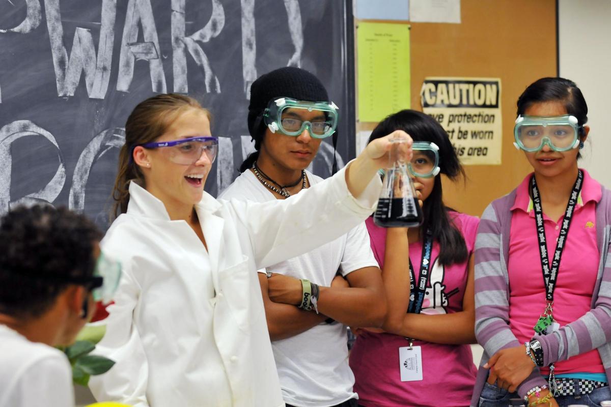 a girl holds up a flask as her class conducts a science experiment