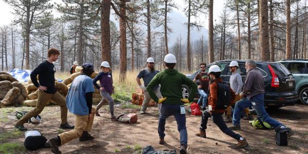 A group of volunteers do lunges in a circle with hard hats on