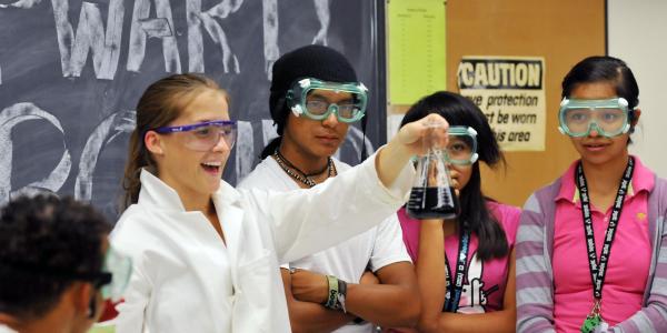 a girl holds up a flask as her class conducts a science experiment
