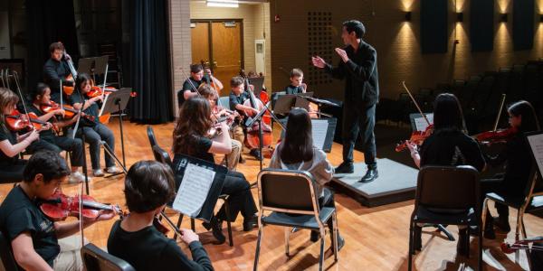 CU Boulder student leads a strings ensemble of middle school students in practice